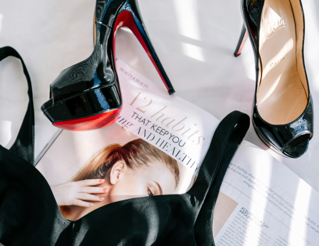 An image of a pair of Christian Louboutin shoes positioned on a white background, accompanied by a stylish purse and a fashion magazine