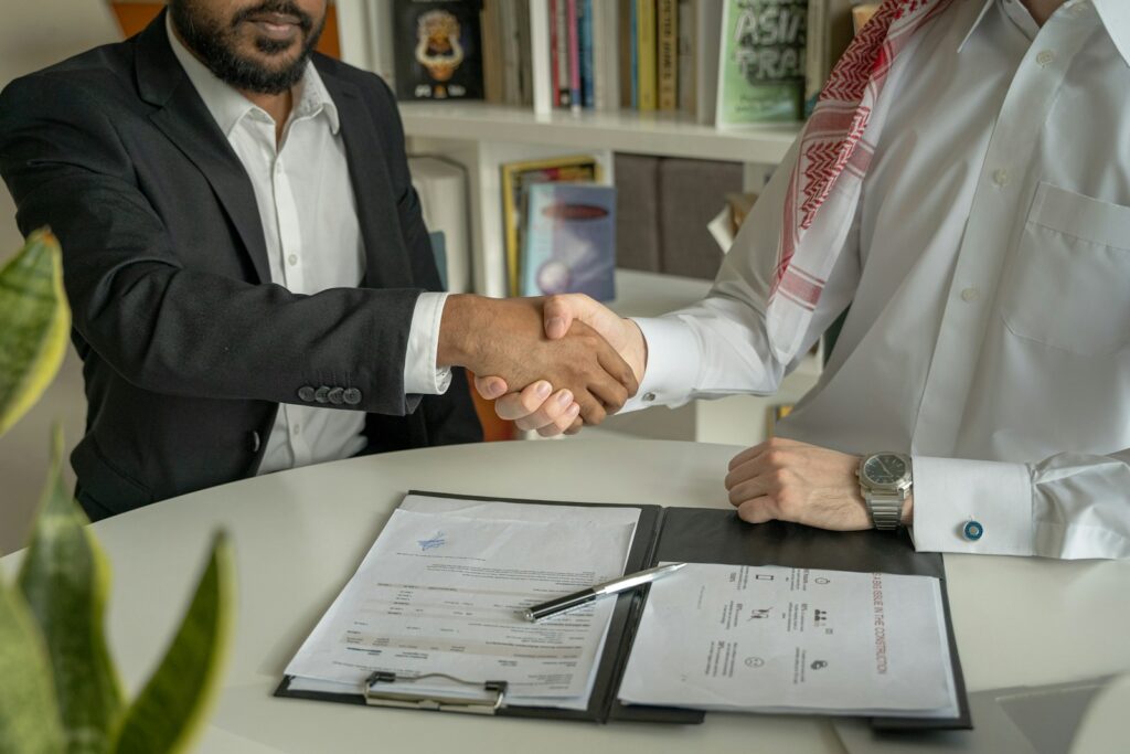 a couple of men shaking hands over a desk with a document in front of them
