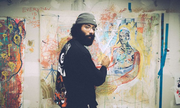 man in black and white sweater standing beside wall with graffiti